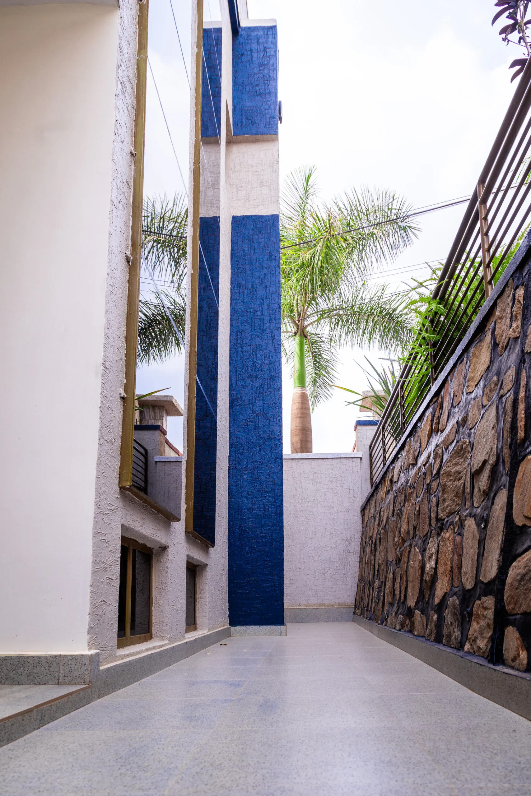 Sendero exterior junto a una vivienda moderna con muro de piedra y vegetación tropical.