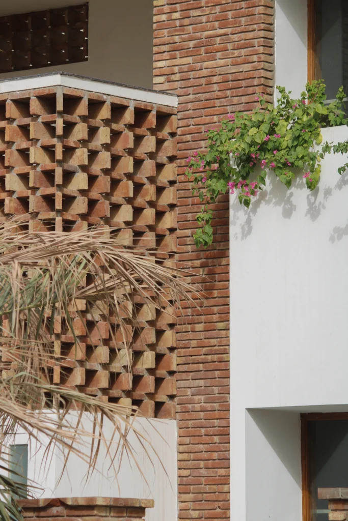 Fachada de ladrillo texturizado, muro blanco y bugambilia como referencia de materiales y clima.