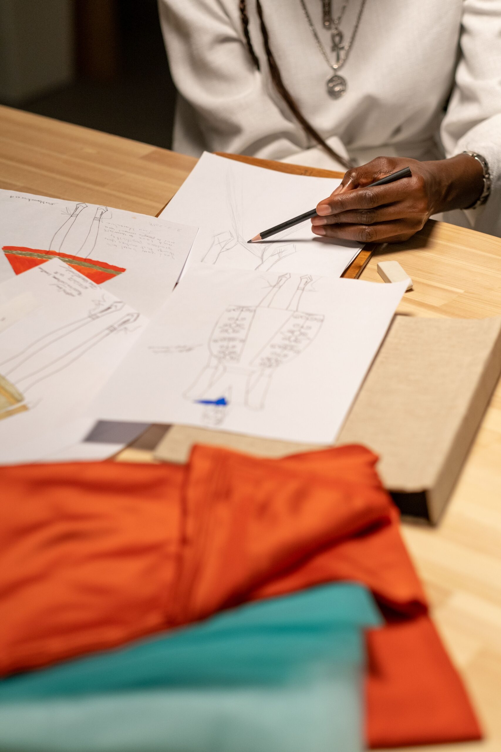 Diseñadora trabajando con bocetos de prendas y muestras textiles sobre una mesa