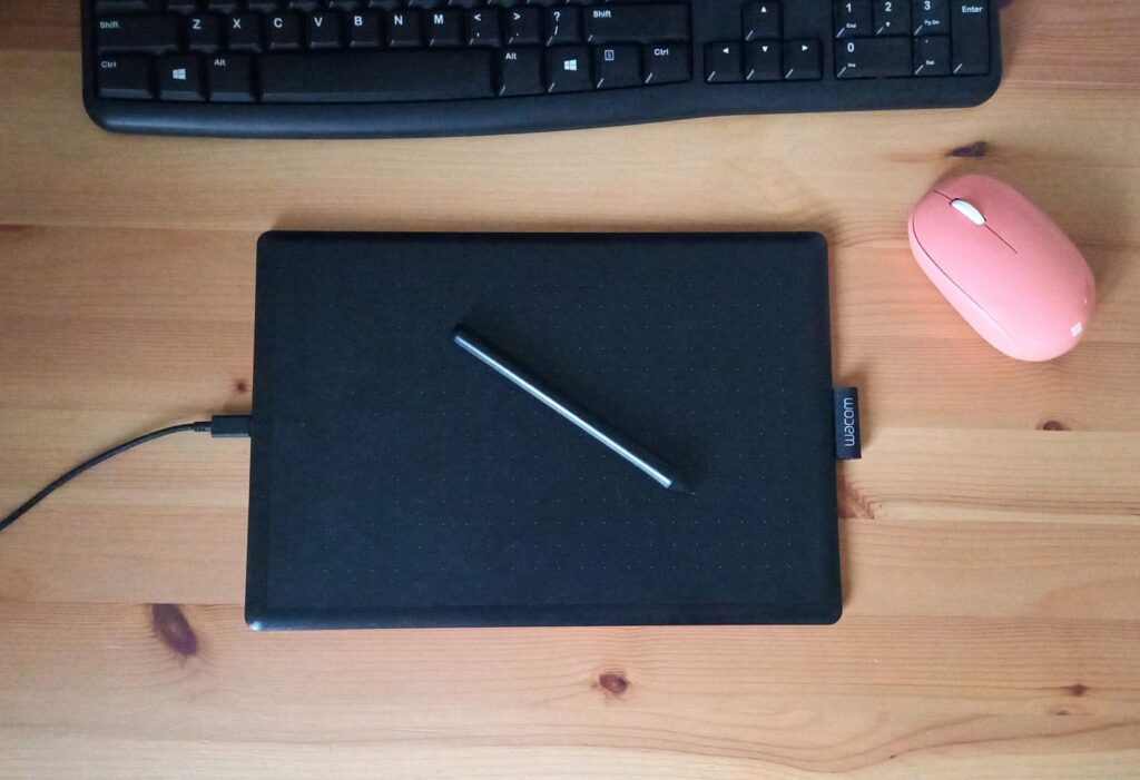 Tableta gráfica con lápiz, teclado y mouse sobre un escritorio de madera