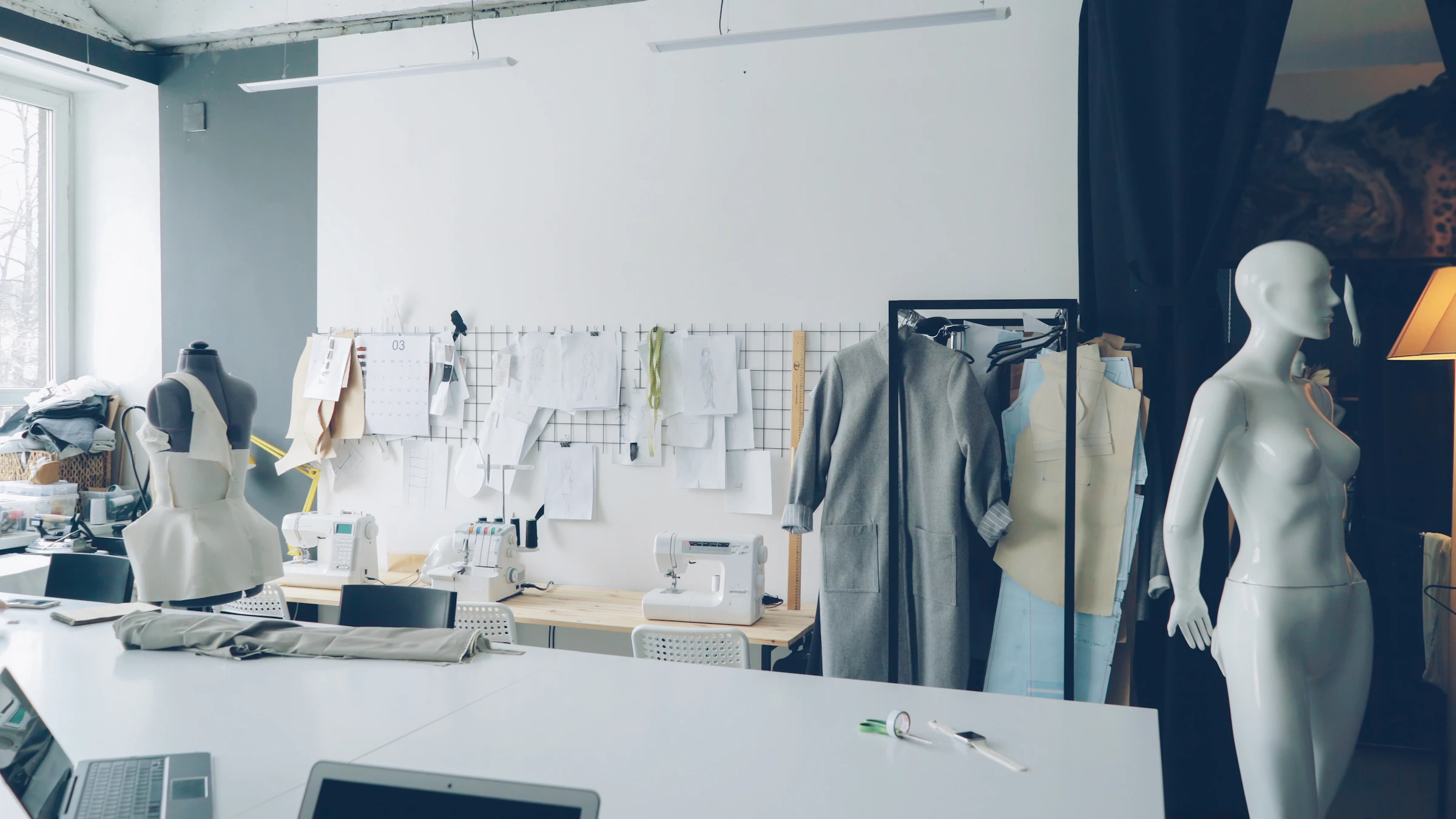 Estudio de diseño de moda con mesa de trabajo, maniquíes, bocetos y máquinas de coser