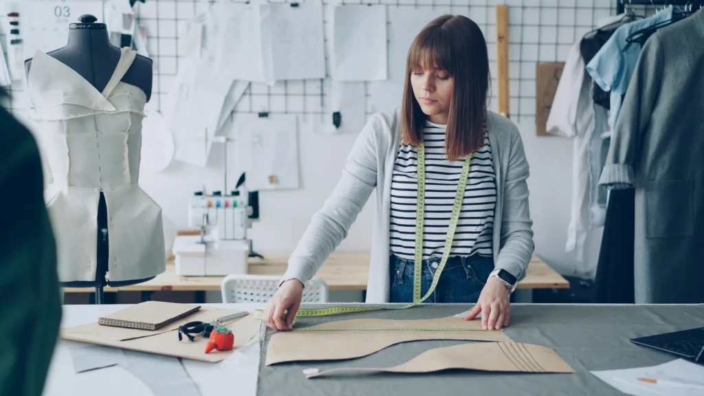 Diseñadora de moda mide patrones de papel sobre una mesa de taller