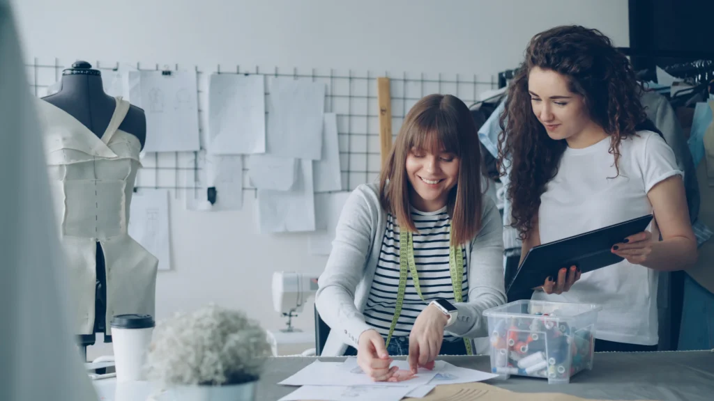 Dos diseñadoras revisan bocetos y una tableta en un taller de moda