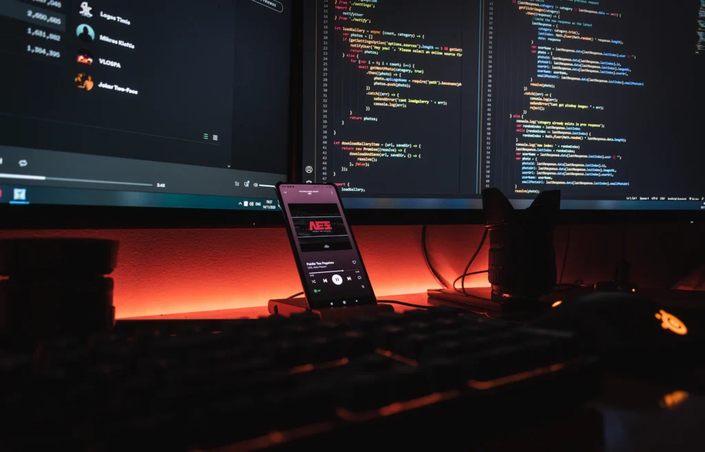 Monitores con código y un teléfono sobre el escritorio de una persona desarrolladora
