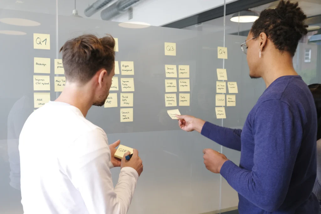 Dos personas organizando un plan de proyecto con notas adhesivas sobre un muro de cristal