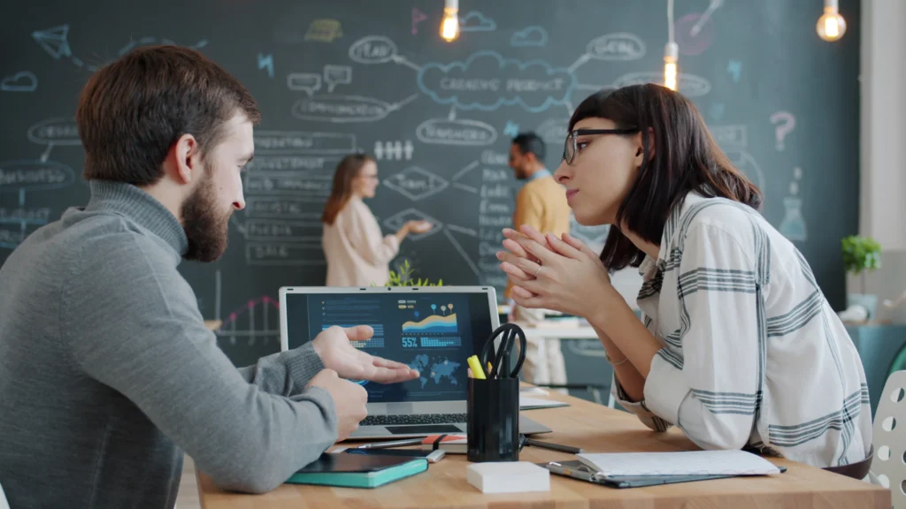 Dos colegas revisando gráficas de datos en una computadora portátil